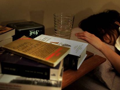 Una mujer durmiendo, con varios libros en la mesilla, junto al reloj despertador. 