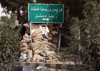 Una foto del presidente sirio Bachar el Asad cuelga de un muro de sacos colocados por el Ej&eacute;rcito cerca de la ciudad de Harasta, nueve kil&oacute;metros al norte de Damasco.