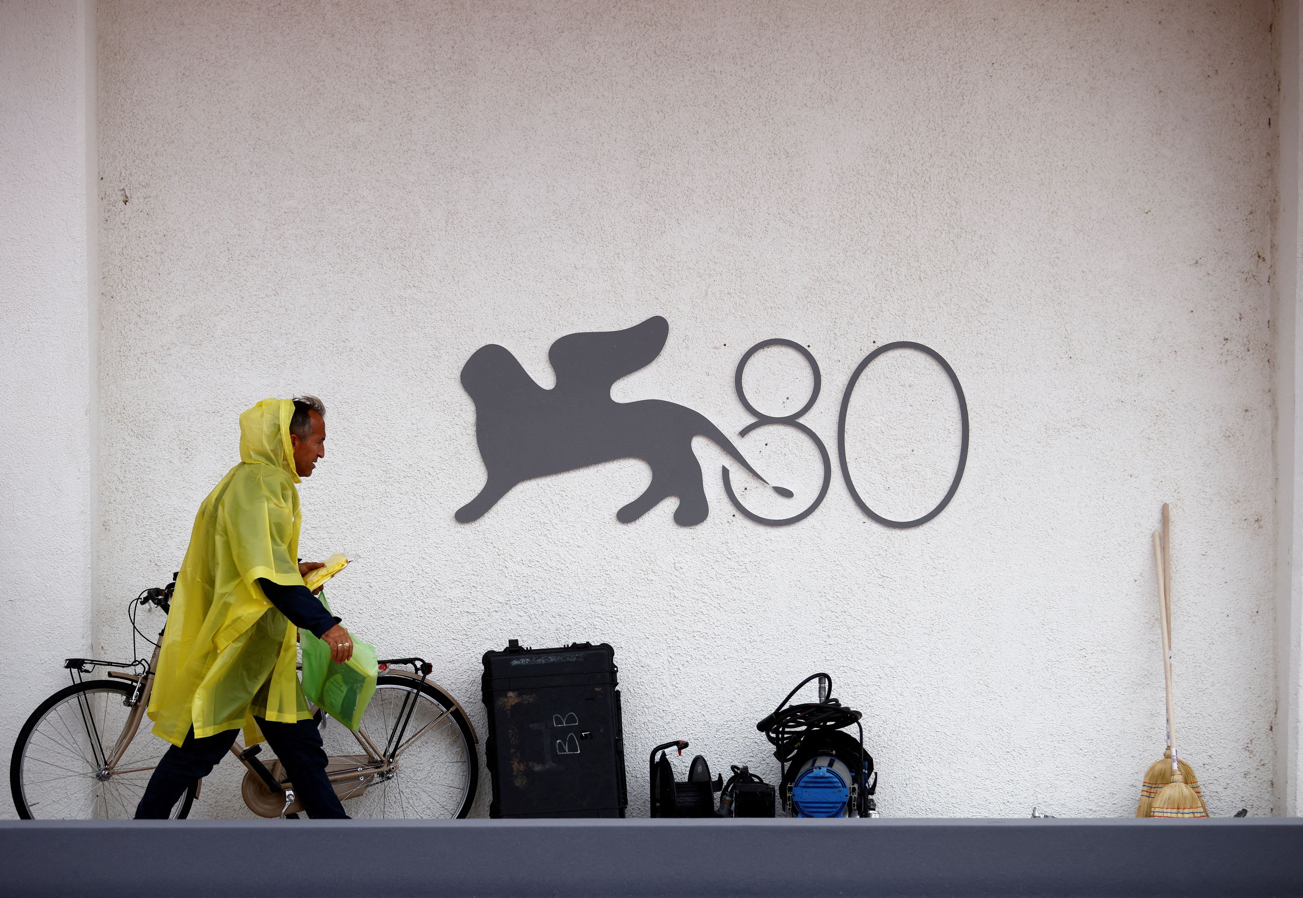 Un hombre pasea bajo la lluvia delante del logotipo del 80º festival de cine de Venecia este martes, un día antes de su inauguración.