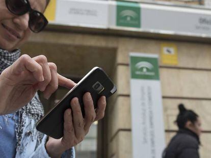 Una mujer usa un móvil en la puerta de una oficina de empleo en Sevilla.
 