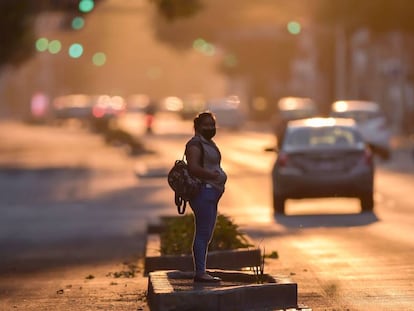 Una mujer con una mascarilla espera sobre una avenida de Ciudad de México. 
 
 