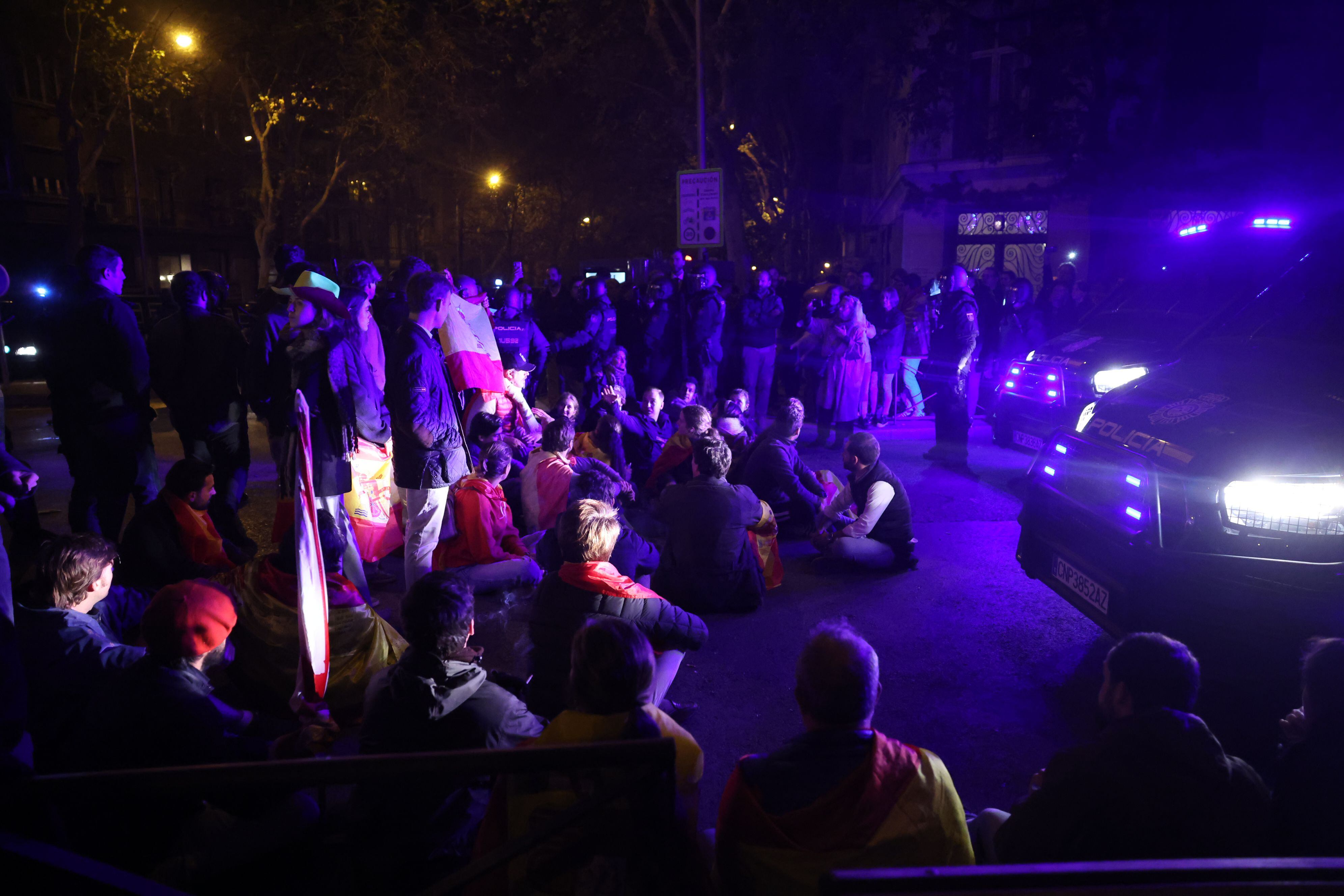 Un grupo de manifestante realiza una sentada frente a los furgones policiales. 