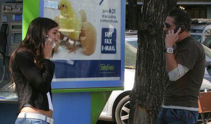 Dos j&oacute;venes hablan por un tel&eacute;fono m&oacute;vil junto a una cabina telef&oacute;nica. 