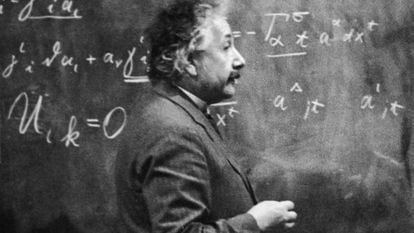 El físico Albert Einstein (1879 - 1955) de pie junto a una pizarra con cálculos matemáticos escritos con tiza.