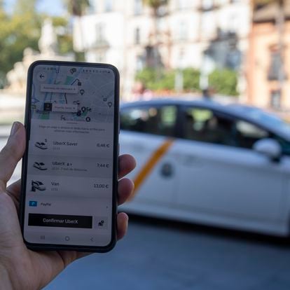 Imagen de un móvil con la app de Uber y un taxi de fondo, el día en que se aprobará el decreto para regular las VTC en Andalucía (septiembre de 2022).