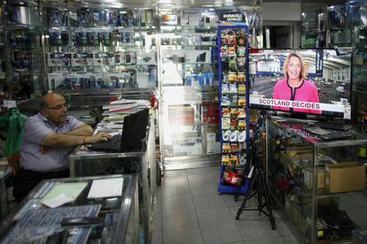 Un vendedor trabaja con su portátil mientras un periodista informa en la televisión sobre el referéndum de Escocia, en una tienda de electrónica en el centro de Gibraltar.