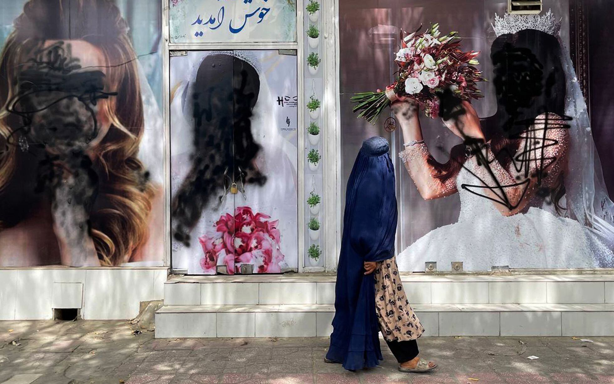 Una afgana ataviada con el burka pasa ante los carteles de un centro de belleza, vandalizados con pintura negra, el 20 de agosto de 2021 en Kabul.