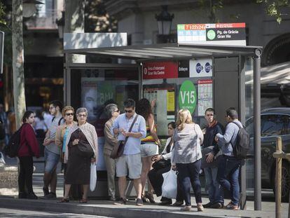Ciudadanos y turistas esperan en una de las paradas del paseo de Gràcia que van al Park Güell.