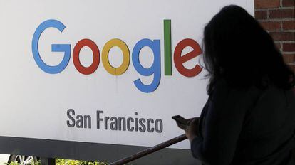 Una persona consulta su móvil junto a un cartel de Google.