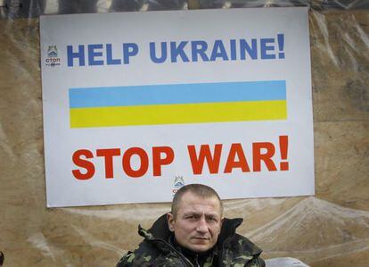 Un veterano del Maidan ante un cartel que dice: &quot;Ayuden a Ucrania, paren la guerra&quot;.