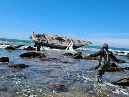 Unas personas se acercan al velero 'Capitán III' embarrancado en el arrecife de Salmedina, Cádiz.