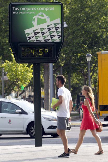 Dos personas pasan por delante de un termómetro en Zaragoza.