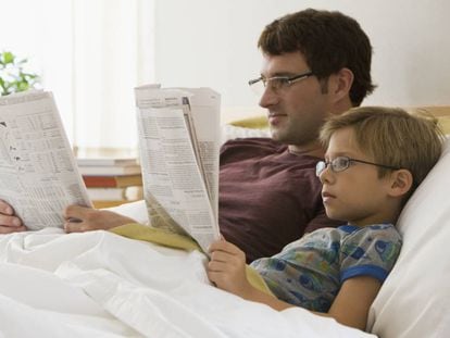 Un padre y su hijo leen el periódico en la cama.