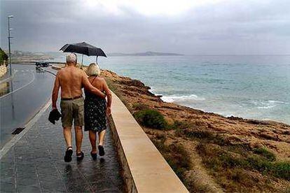 Dos paseantes por el litoral marítimo de Tarragona, con calor y protegiéndose con un paraguas de la lluvia.