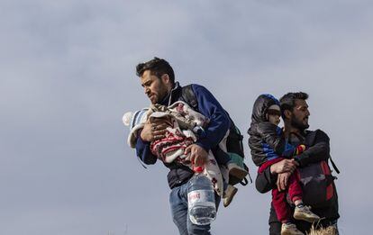 Dos migrantes con sus hijos en brazos cruzan la ciudad de Edirne (Turquía), en su travesía hacia Grecia, el 3 de marzo. 