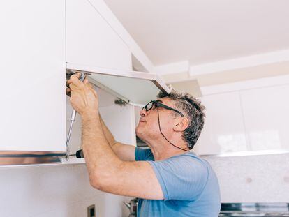 Un hombre repara un mueble de cocina.