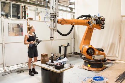 An IAAC student next to a robotic arm dedicated to 3D printing.