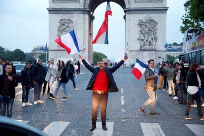 Un hombre grita mientras agita una bandera nacional francesa en la avenida de los Campos Elíseos con el Arco del Triunfo detrás.