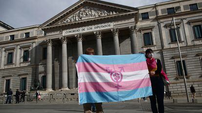 Dos personas sostienen una bandera 'trans' frente al Congreso de los Diputados.