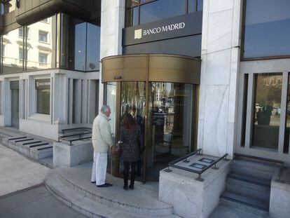 Una pareja de clientes habla con un guarda de seguridad en la sede del Banco Madrid que desde hoy permanece cerrada al público.