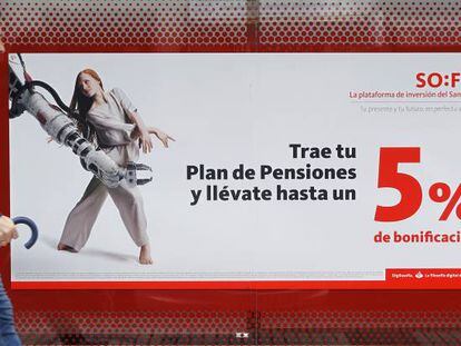 Una persona camina delante de una sucursal bancaria en la que se anuncian planes de pensiones. 
