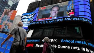 La gente pasa caminando mientras el gobernador de Nueva York, Andrew Cuomo, transmite en vivo su discurso de despedida en una pantalla en Times Square, Nueva York, el 23 de agosto de 2021. En vídeo, una parte del discurso de Cuomo.