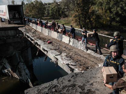 Voluntarios ucranios cruzan cajas de comida a través de un puente destrozado sobre el río Oskil (en el este de Ucrania) recientemente recuperado.