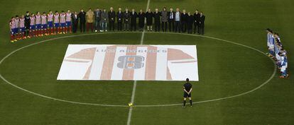 Los jugadores del Atlético, Real Sociedad y exjugadores colchoneros en el centro del campo con una pancarta con la camiseta de Luis Aragones