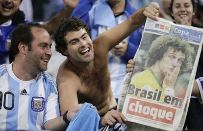 Dos aficionados argentinos se recrean con la eliminaci&oacute;n de Brasil mostrando un peri&oacute;dico local en las gradas del Arena Corinthians de S&atilde;o Paulo