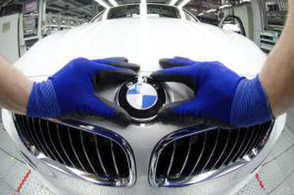 Un empleado colocando el logo de BMW en el capó de un coche nuevo en la fábrica de Regensburgo (Alemania). EFE/Archivo