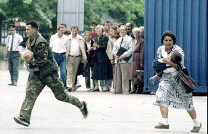 Un soldado bosnio, con un niño en brazos, y una mujer que porta a otro cruzan una calle a la carrera para evitar los disparos de los francotiradores de Sarajevo.