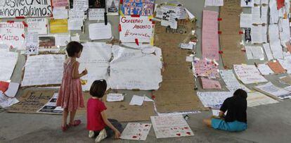 Tres niños observan en Sevilla los carteles dejados por acampados del movimiento 15-M.