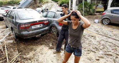 Dos vecinos de Vera (Almer&iacute;a) caminan entre lodo junto a varios veh&iacute;culos arrastrados en las inundaciones. 