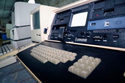 En primer plano, la primera microcomputadora portátil Osborne 1, del año 1981 y 11 kg de peso.