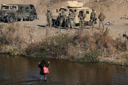 Una migrante cruza el Río Bravo con las manos en alto, frente a la valla de púas colocada por agentes de la Guardia Nacional de Texas.
