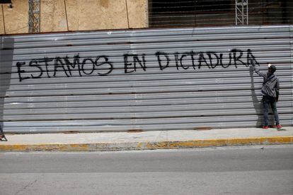 Un hombre pinta un grafiti sobre una pared donde se puede leer 'Estamos en dictadura'.
