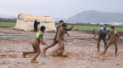 Un grupo de sirios desplazados por la ofensiva contra la provincia rebelde de Idlib (noroeste) juegan este jueves al fútbol en un campo embarrado en Sarmada.