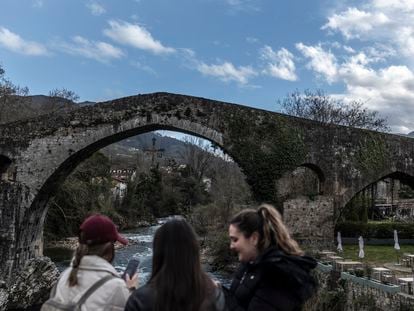 Tres jóvenes miran en sus teléfonos las fotos que se han hecho, en el puente romano de Cangas de Onís.