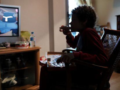 Un niño ve la tele mientras come un trozo de pizza del menú infantil que se entregó en la Comunidad de Madrid durante el confinamiento a menores que recibían una beca comedor, en marzo de 2020.