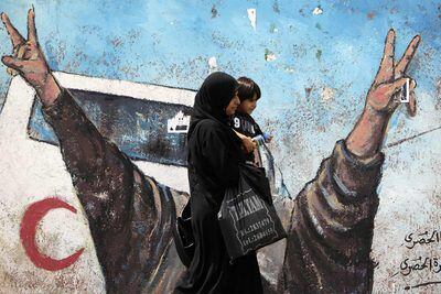 Una mujer con su hijo pasa junto a un mural antiisraelí en una calle de Gaza.