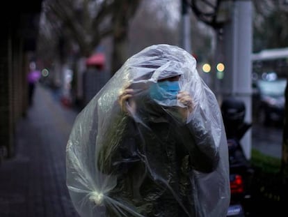 Un hombre con máscara y cubierto por plástico en Shanghái, China.