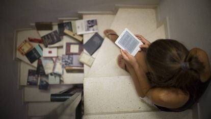 Una joven lee un libro electrónico junto a varios libros en papel.