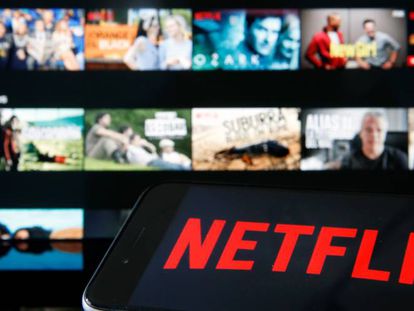 Logo de Netflix en un móvil con imágenes de películas y series de fondo.