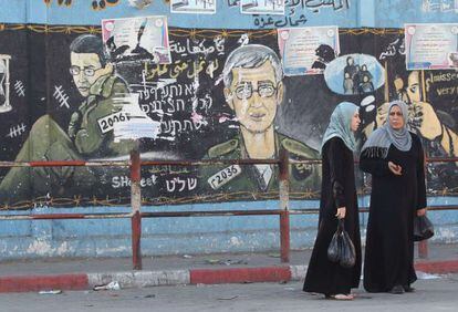 Mujeres palestinas caminan junto a un mural en el norte de Gaza en el que parecen imágenes del soldado Shalit en Gaza.