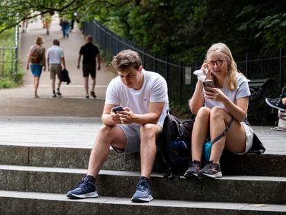 Dos personas miran el móvil mientras están en un parque.