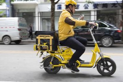 Un mensajero de Waimai comprueba la dirección a la que lleva comida a domicilio a bordo de una bicicleta eléctrica.