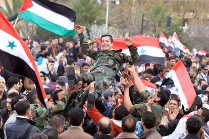 Simpatizantes del r&eacute;gimen sirio, con banderas sirias y palestinas, mantean a un joven soldado en la manifestaci&oacute;n celebrada el jueves en Damasco.