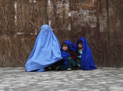 Una mujer afgana vestida con un burka y sus hijos esperan el autobús en Kabul (Afganistán).