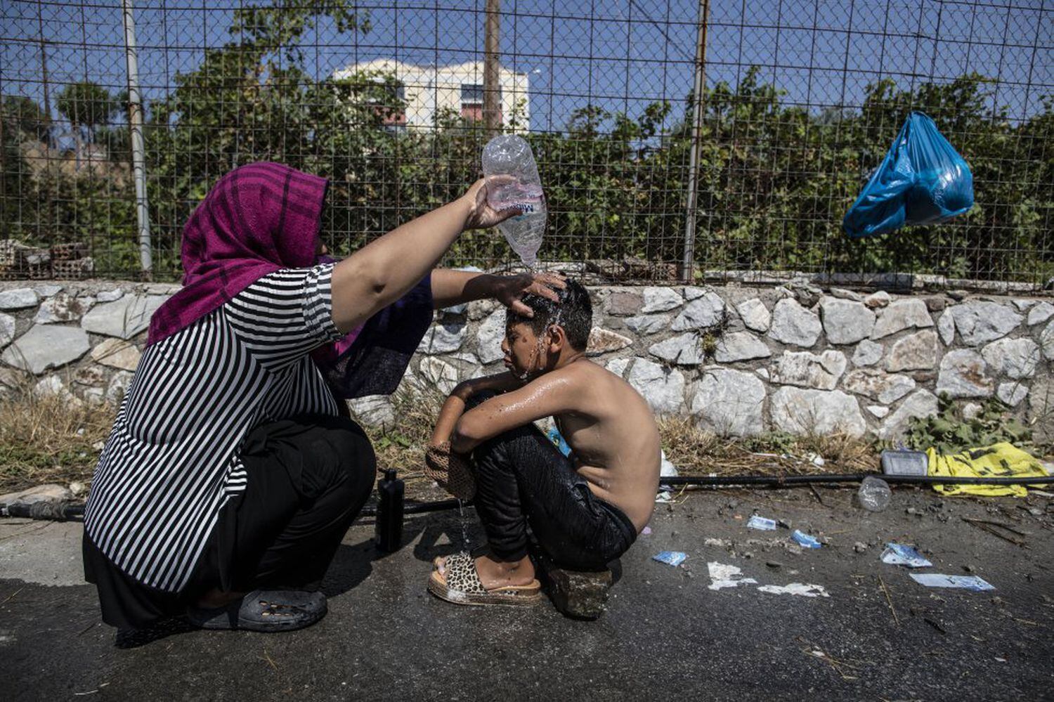 Μια γυναίκα πρόσφυγας πλένει ένα αγόρι με ένα μπουκάλι νερό στον αυτοσχέδιο χώρο στάθμευσης δίπλα σε ένα σούπερ μάρκετ στη Μυτιλήνη της Λέσβου.