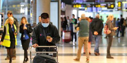 Un viajero, recién llegados al aeropuerto de Manises, consulta su móvil protegido con una mascarilla. 